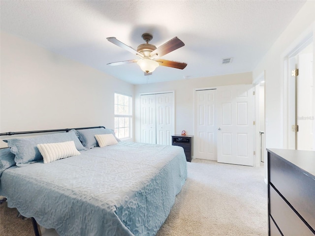 carpeted bedroom featuring multiple closets, a textured ceiling, and ceiling fan