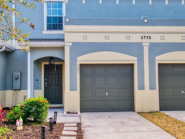 2775 Revolution St Unit 103, Melbourne, FL 32935 - doorway to property featuring an attached garage, concrete driveway, and stucco siding