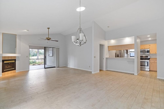 unfurnished living room with light hardwood / wood-style floors, ceiling fan with notable chandelier, a tiled fireplace, and vaulted ceiling