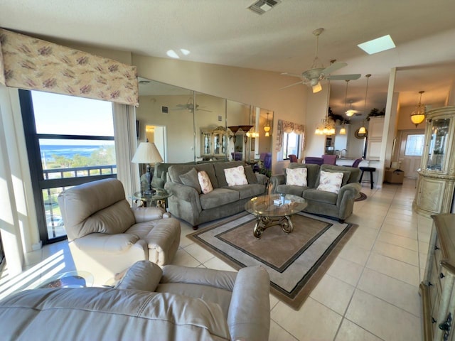 tiled living room featuring ceiling fan with notable chandelier, a textured ceiling, and high vaulted ceiling