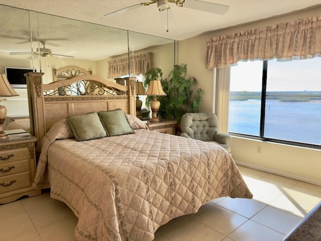 bedroom with ceiling fan, a water view, light tile patterned floors, and a textured ceiling