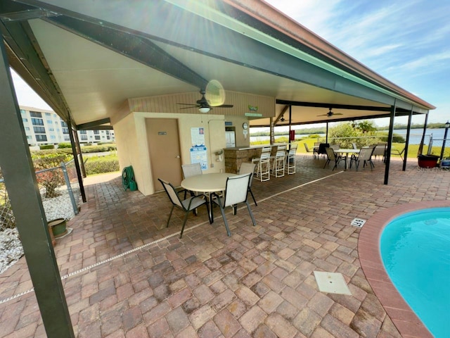 view of patio featuring ceiling fan, an outdoor bar, a community pool, and a water view