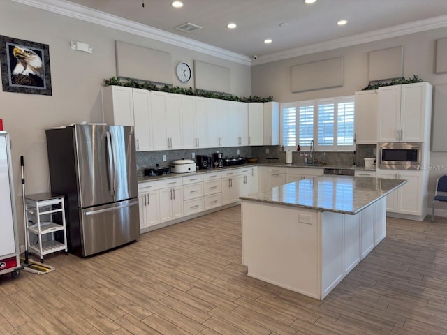 kitchen with white cabinetry, stainless steel appliances, a kitchen island, and light stone counters