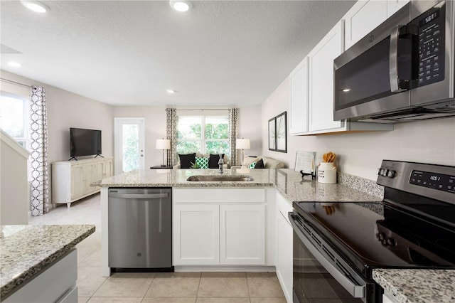 kitchen with kitchen peninsula, sink, stainless steel appliances, white cabinets, and light stone counters