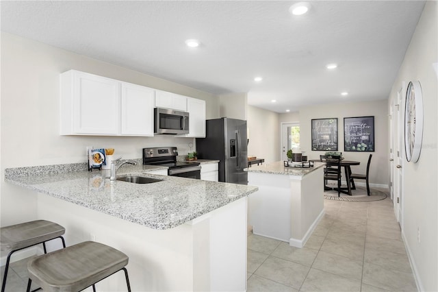 kitchen featuring kitchen peninsula, appliances with stainless steel finishes, light stone countertops, a kitchen island, and sink