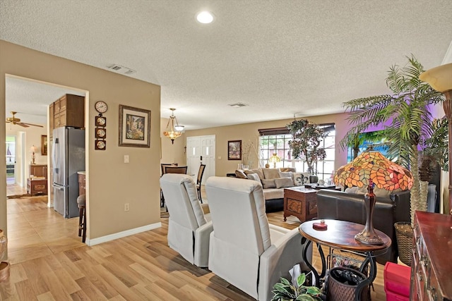 living room with ceiling fan, a textured ceiling, and light hardwood / wood-style flooring