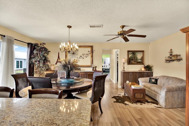 dining room with ceiling fan with notable chandelier, light hardwood / wood-style flooring, and a textured ceiling