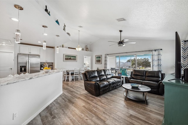 living room featuring ceiling fan, hardwood / wood-style floors, vaulted ceiling, and a textured ceiling