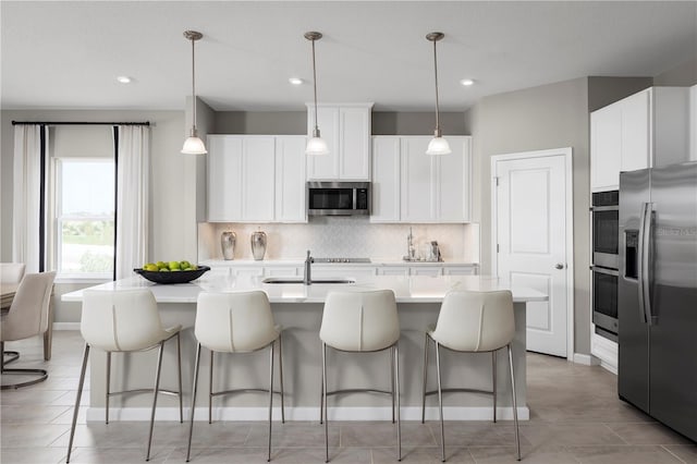 kitchen with hanging light fixtures, appliances with stainless steel finishes, white cabinetry, and a center island with sink