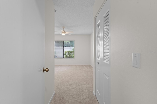 hallway with light carpet and a textured ceiling