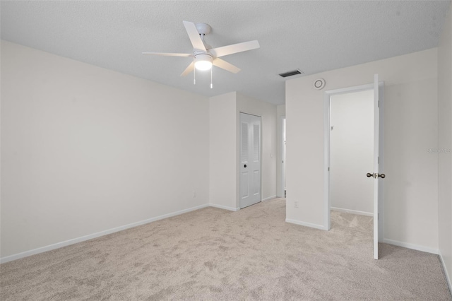 unfurnished bedroom featuring ceiling fan, a textured ceiling, a closet, and light carpet