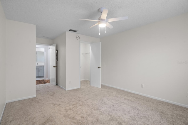 unfurnished bedroom with a spacious closet, a textured ceiling, a closet, ceiling fan, and light colored carpet