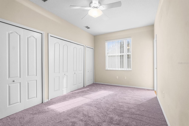 unfurnished bedroom with light carpet, two closets, and ceiling fan