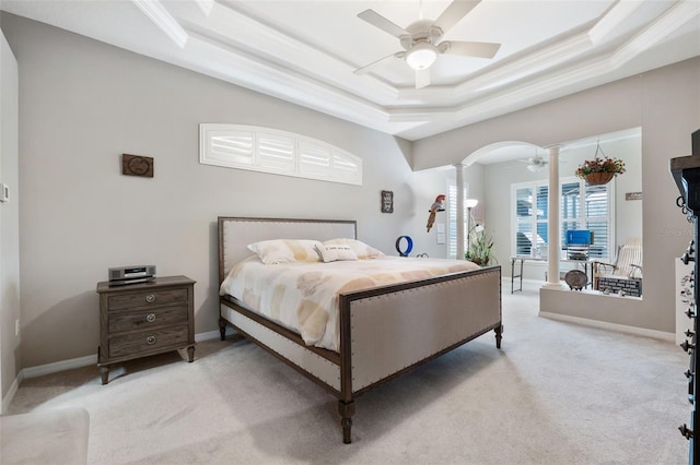 bedroom with decorative columns, light colored carpet, a tray ceiling, and ceiling fan