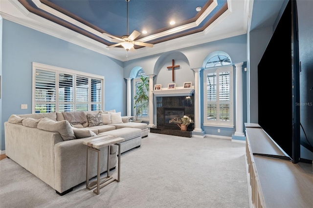 carpeted living room with ornamental molding, ornate columns, ceiling fan, and a raised ceiling