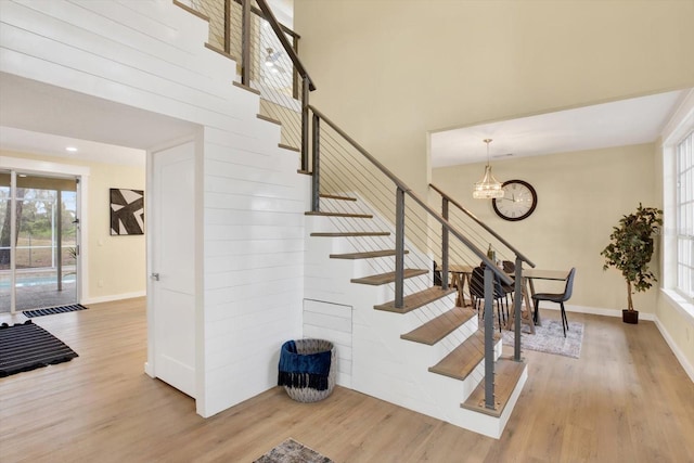 stairway with baseboards, wood finished floors, a towering ceiling, and a notable chandelier