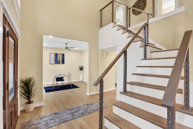 foyer entrance with a high ceiling, wood finished floors, a ceiling fan, baseboards, and stairway