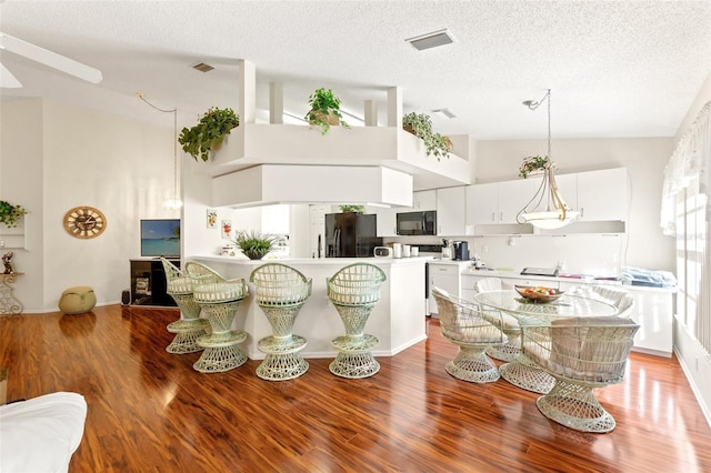 dining area featuring high vaulted ceiling, a textured ceiling, and light wood-type flooring