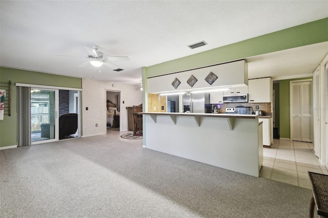 kitchen with ceiling fan, a breakfast bar, kitchen peninsula, white cabinetry, and stainless steel appliances