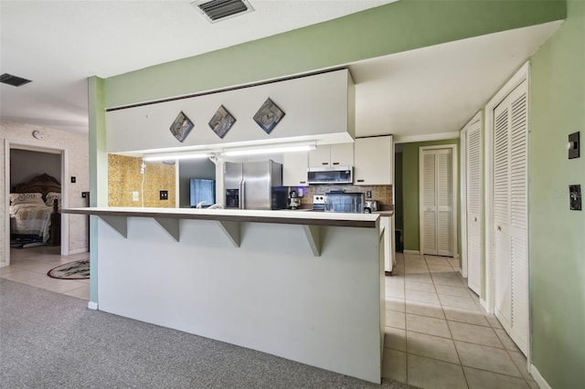 kitchen with kitchen peninsula, light tile patterned floors, appliances with stainless steel finishes, a kitchen breakfast bar, and white cabinets