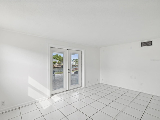 spare room featuring french doors, light tile patterned floors, and a water view