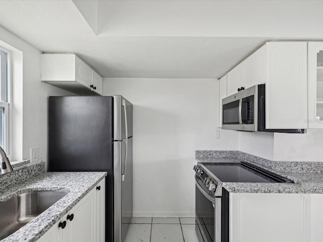 kitchen featuring appliances with stainless steel finishes, light tile patterned flooring, white cabinets, light stone counters, and sink