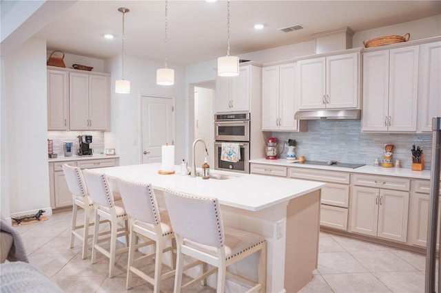 kitchen featuring pendant lighting, sink, a kitchen island with sink, black electric cooktop, and decorative backsplash