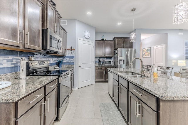 kitchen with sink, light tile patterned floors, appliances with stainless steel finishes, pendant lighting, and a kitchen island with sink