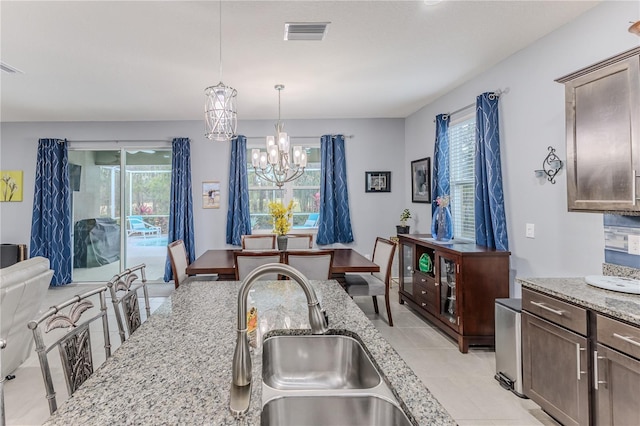 kitchen with sink, dark brown cabinetry, light stone countertops, decorative light fixtures, and a chandelier