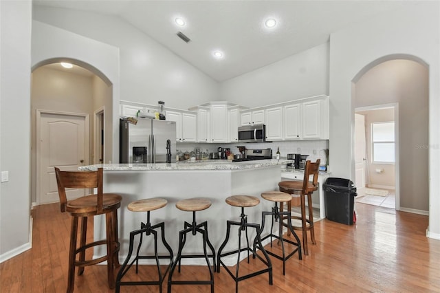 kitchen with appliances with stainless steel finishes, light wood-type flooring, white cabinetry, a kitchen bar, and high vaulted ceiling