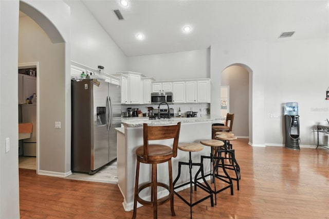 kitchen with light stone countertops, white cabinets, stainless steel appliances, decorative backsplash, and high vaulted ceiling