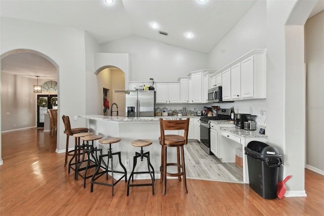 kitchen featuring white cabinets, light stone countertops, a center island with sink, decorative backsplash, and stainless steel appliances