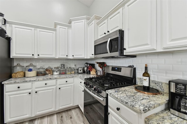 kitchen with white cabinets, appliances with stainless steel finishes, tasteful backsplash, light hardwood / wood-style floors, and light stone counters