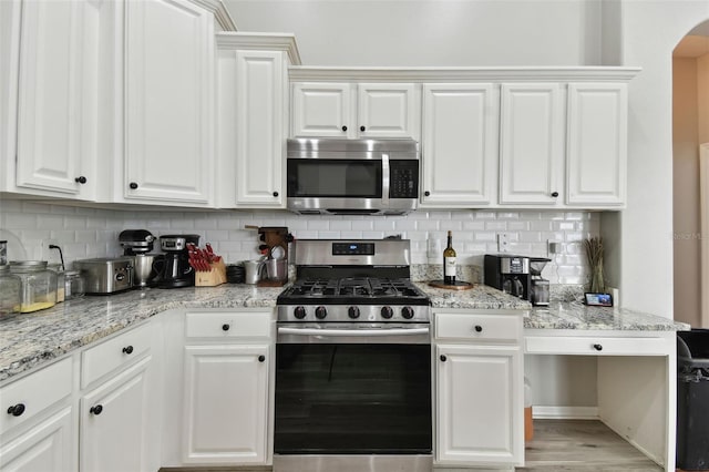 kitchen with light hardwood / wood-style floors, white cabinets, backsplash, stainless steel appliances, and light stone counters