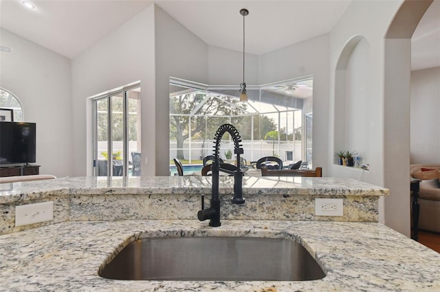 kitchen featuring sink, pendant lighting, lofted ceiling, and light stone countertops