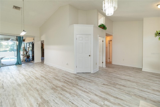 unfurnished living room featuring high vaulted ceiling, an inviting chandelier, and light hardwood / wood-style floors