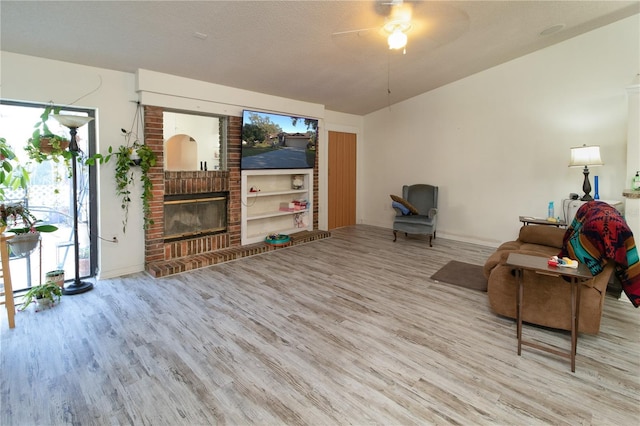 sitting room with light hardwood / wood-style flooring, ceiling fan, a fireplace, a textured ceiling, and vaulted ceiling