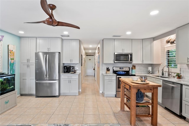 kitchen featuring stainless steel appliances, sink, backsplash, light stone counters, and light tile patterned floors