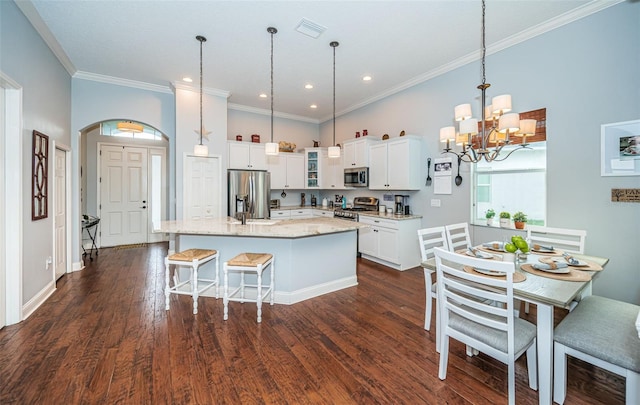 kitchen with stainless steel appliances, a center island with sink, white cabinets, and decorative light fixtures