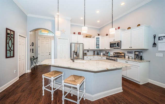 kitchen featuring white cabinetry, appliances with stainless steel finishes, pendant lighting, light stone countertops, and a kitchen island with sink