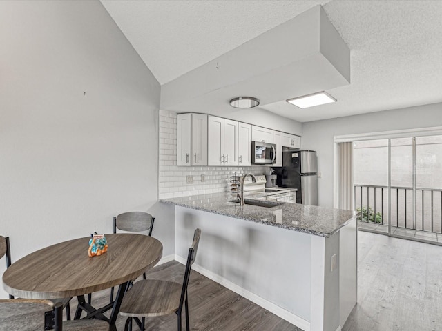 kitchen featuring stone counters, appliances with stainless steel finishes, white cabinetry, decorative backsplash, and kitchen peninsula