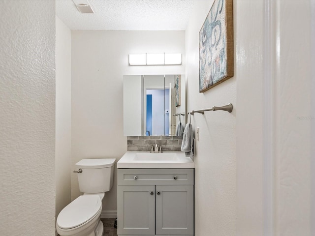 bathroom with vanity, decorative backsplash, toilet, and a textured ceiling