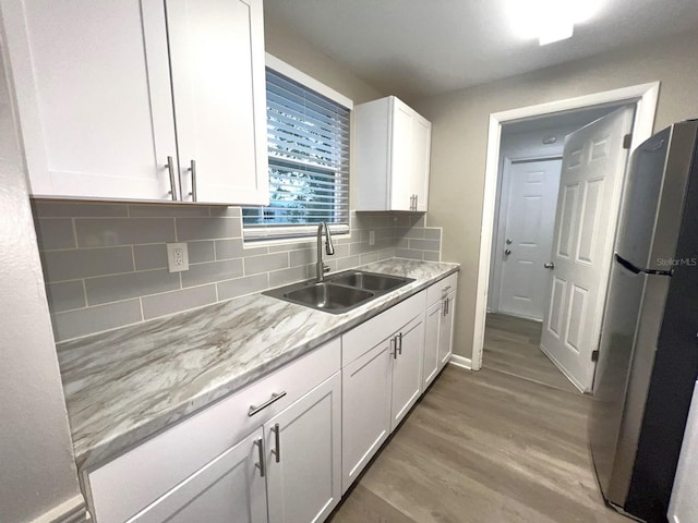 kitchen featuring light hardwood / wood-style floors, tasteful backsplash, stainless steel refrigerator, sink, and white cabinets