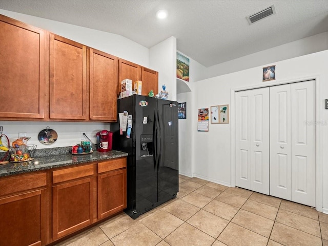 kitchen with a textured ceiling, light tile patterned flooring, black fridge, and dark stone counters