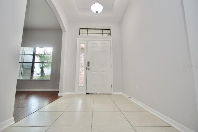 entryway with a raised ceiling and light tile patterned flooring