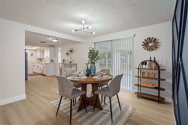 dining room with sink, a chandelier, light hardwood / wood-style flooring, and a textured ceiling