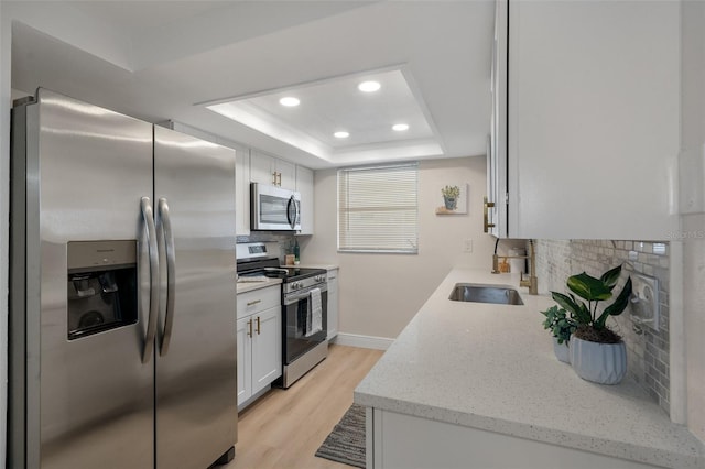 kitchen featuring white cabinetry, stainless steel appliances, light hardwood / wood-style floors, sink, and a raised ceiling