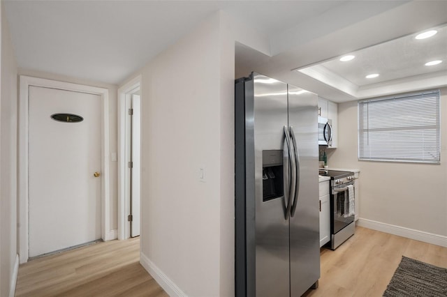 kitchen with light hardwood / wood-style floors, white cabinetry, a raised ceiling, and appliances with stainless steel finishes