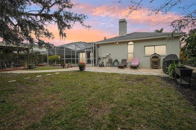 back house at dusk with a patio area, a yard, and a fireplace