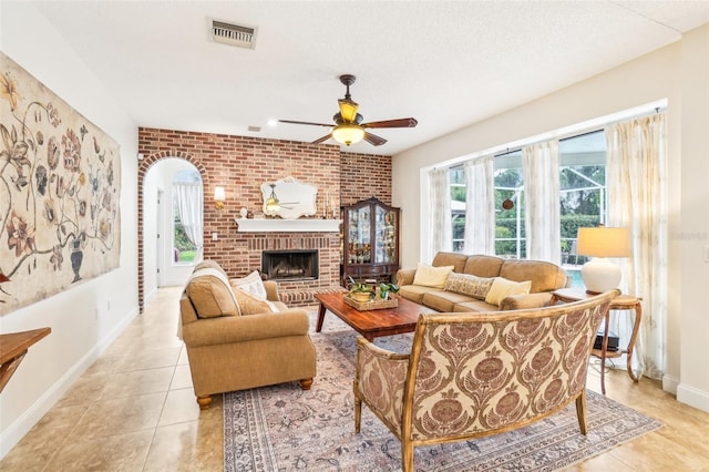 living room with a textured ceiling, a fireplace, brick wall, light tile patterned floors, and ceiling fan